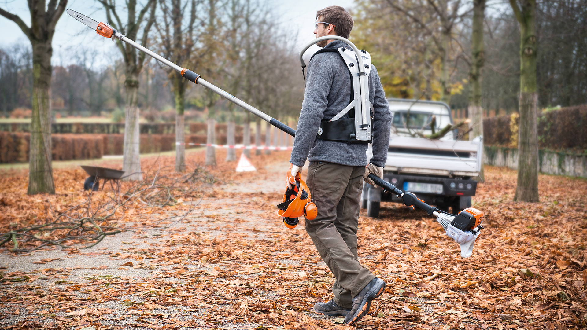 Mann mit STIHL Benzin-Hochentaster HT 133 und Arbeitsfahrzeug im Herbst im Park