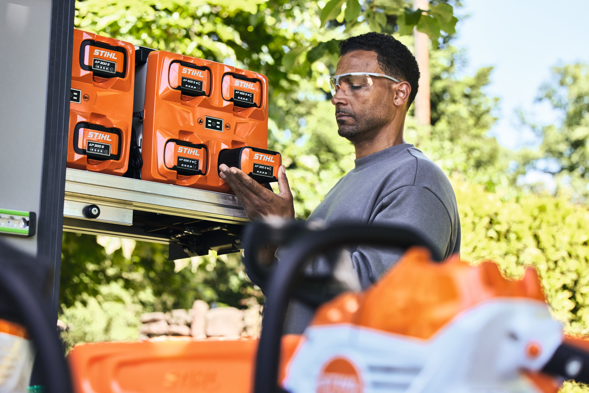 Egy védőszemüveget viselő férfi kiveszi a bottTainer készülékből a STIHL AP 300 S akkumulátort