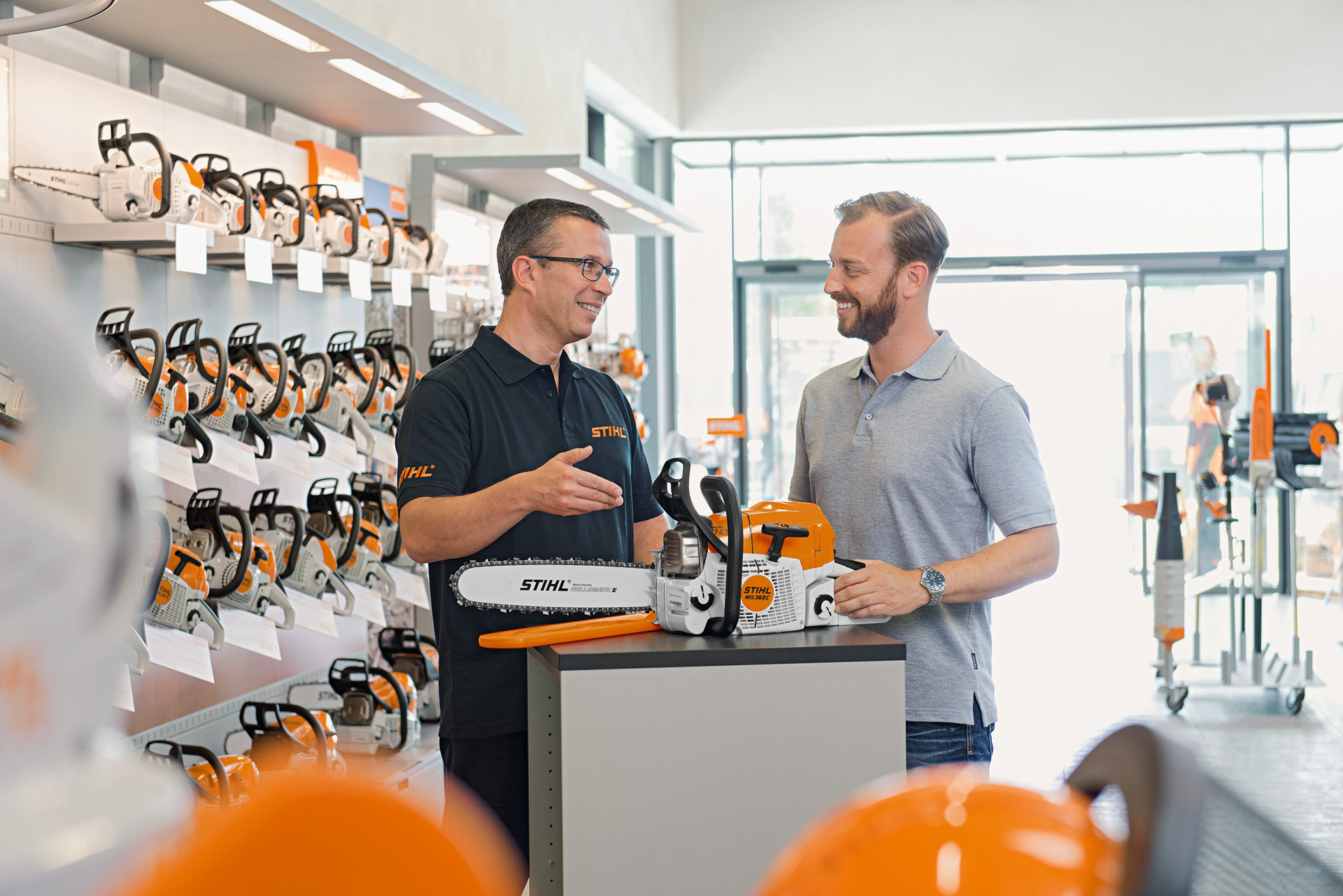 Egy STIHL szakkereskedő tanácsokkal lát el egy fiatal férfit STIHL motorfűrész vásárlása közben