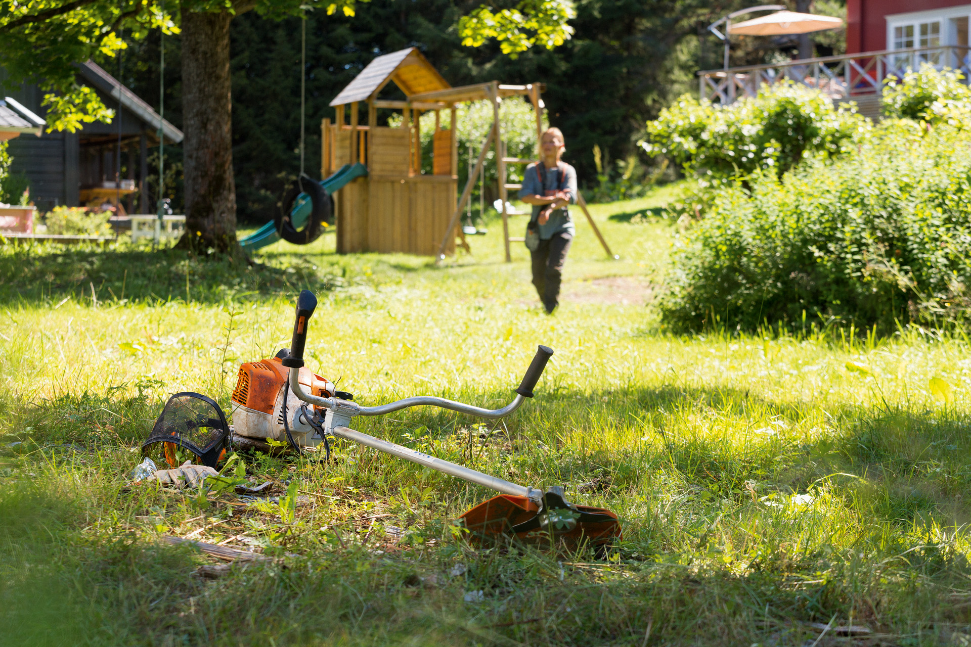 Egy STIHL FS 240 motoros kasza a fűben, a háttérben egy nő készül a karbantartásra 