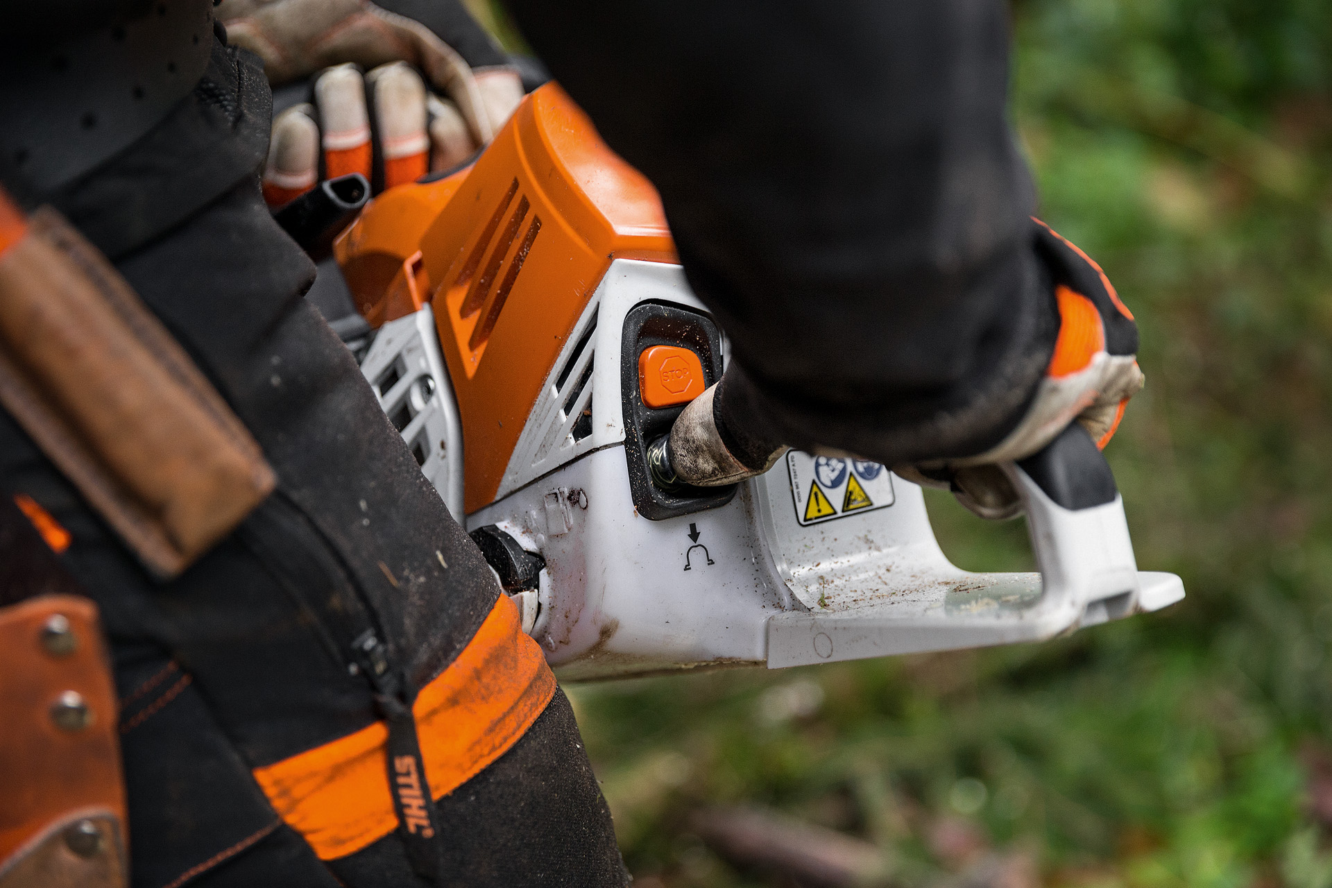 Védőruházatban dolgozó férfi MS 500i STIHL benzines motorfűrészt indít be a földön az erdőben