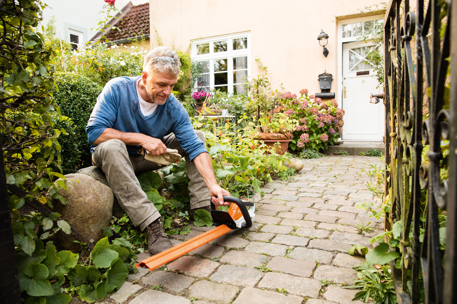 Egy férfi az AI-termékcsalád STIHL HSA 45 elektromos sövénynyírójával egy ház előtt