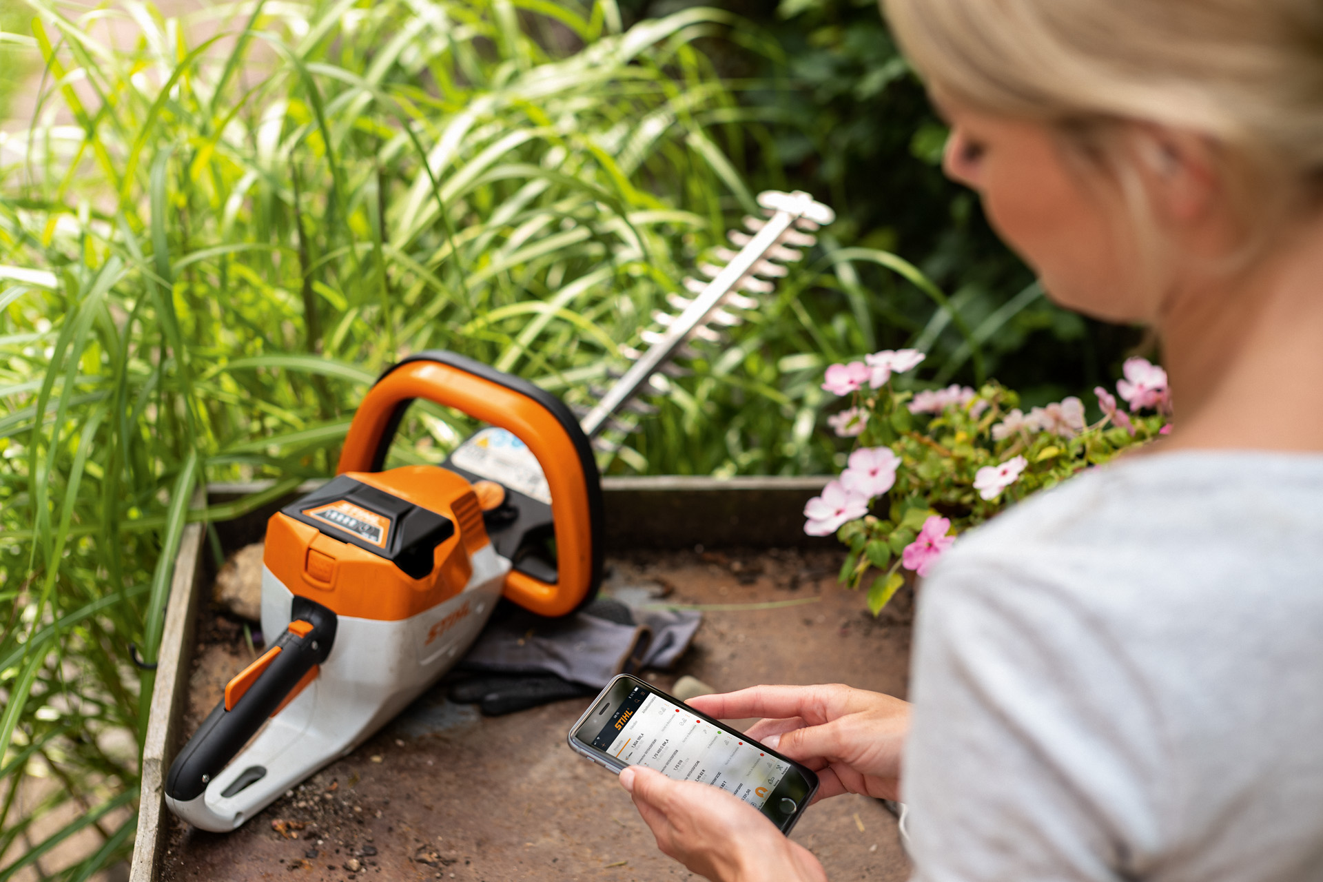 Egy nő STIHL sövénynyíróját a STIHL alkalmazással egy okostelefonon regisztrálja