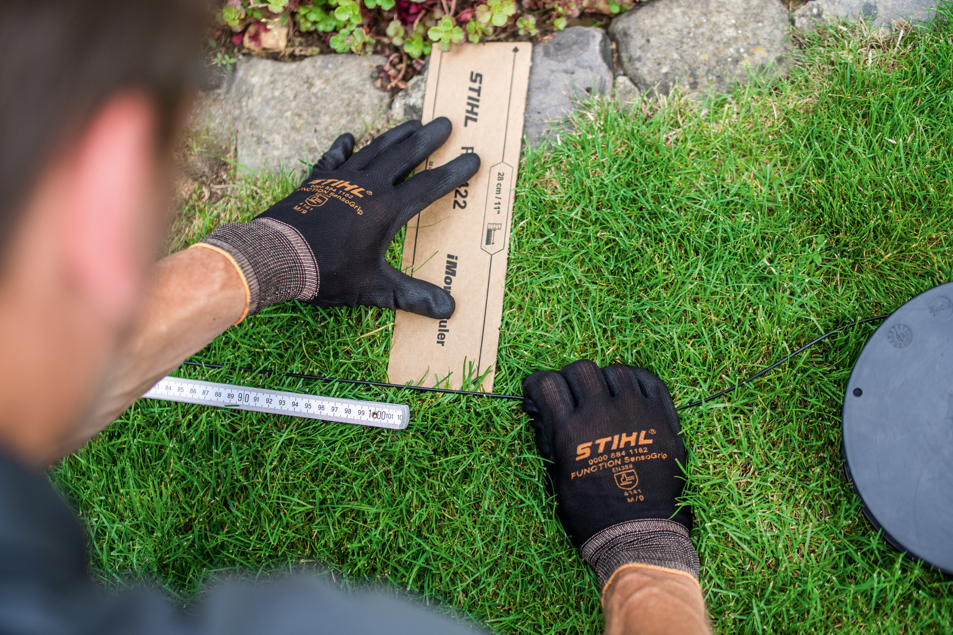 A STIHL szakkereskedő lefekteti a STIHL iMOW robotfűnyíró határolóhuzalát a gyep szélén