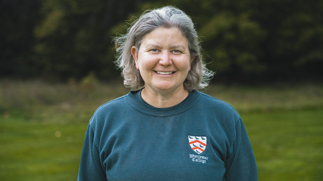 A Worcester College kertépítőjének portréja, aki a szabadban áll a gyepen, professzionális munkaruhát visel.